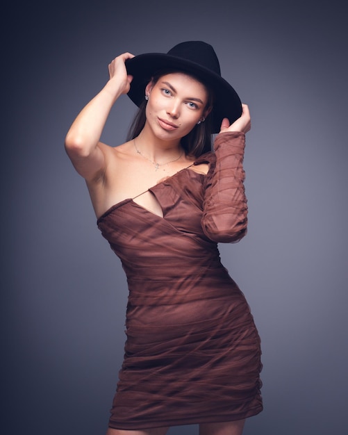 Portrait en studio à la mode d'une belle jeune fille au chapeau noir sur fond gris