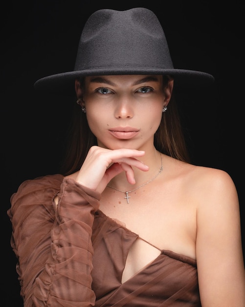 Portrait en studio à la mode d'une belle jeune fille au chapeau noir sur fond noir