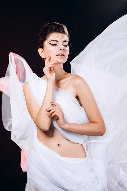 Portrait en studio de mode fille debout enveloppé dans un tissu blanc et touche son visage