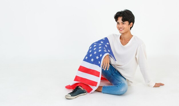 Portrait studio shot of Asian young LGBT gay bisexual homosexual male fashion model in casual outfit sitting smiling using United States of America US national flag cover body on white background