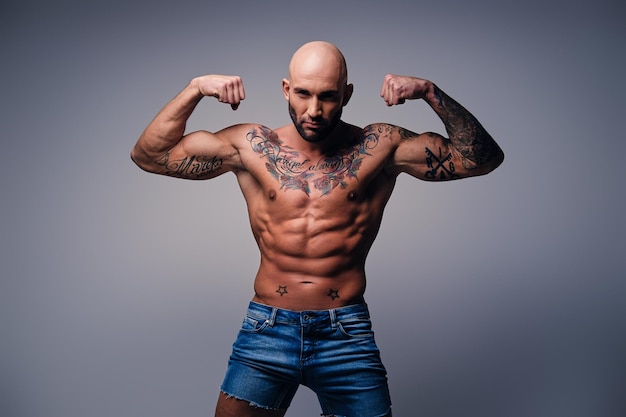 Portrait en studio de tête rasée torse nu, homme musclé avec des tatouages sur son torse sur fond de vignette grise.