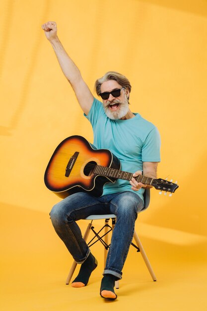 Portrait en studio d'un vieil homme aux cheveux gris portant des lunettes de soleil jouant de la guitare