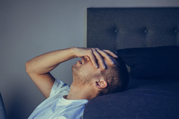 Portrait de style de vie dramatique d'un beau mec dans la trentaine et la quarantaine assis tristement sur le lit, se sentant anxieux et souffrant de dépression Homme séduisant déprimé et bouleversé dans la chambre de la maison