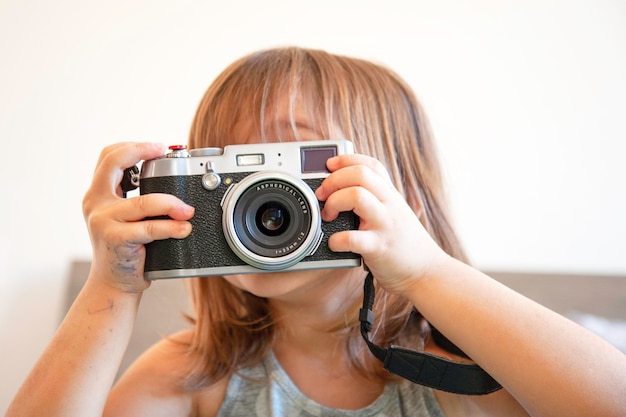 Portrait de style de vie intérieur d'une jolie petite fille faisant une photo Une petite fille talentueuse s'amuse avec un appareil photo vintage Petite fille à la mode faisant une photo à la maison Activité de loisirs à la maison Jeune talent féminin