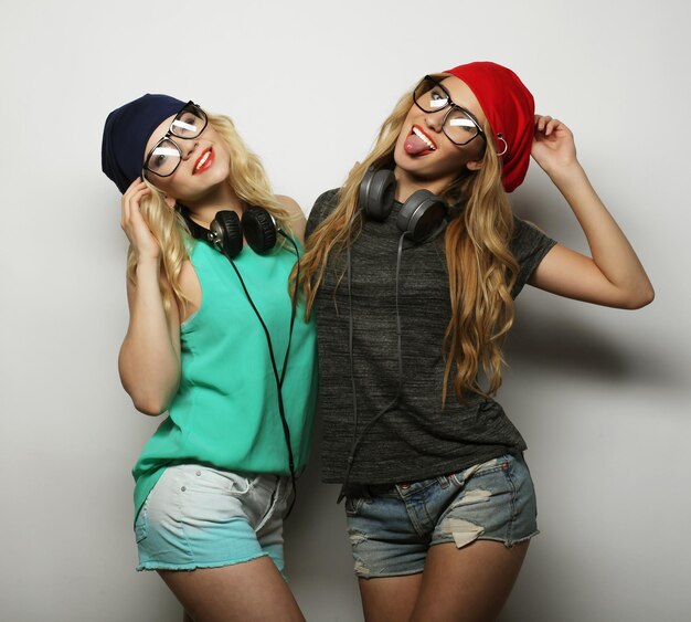 Portrait de style de vie en studio de deux meilleures amies filles hipster portant des tenues lumineuses élégantes, des chapeaux, des shorts en jean et des lunettes devenant fous et s'amusant ensemble Jeune et beauté