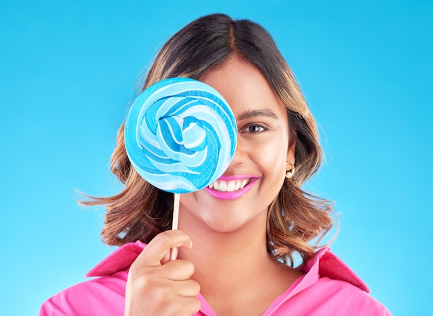 Portrait de sucette ou de femme heureuse sur un fond bleu en studio avec du sucre positif ou un sourire joyeux Bonbons colorés affamés ou visage de fille indienne mangeant une collation géante ou des bonbons avec joie