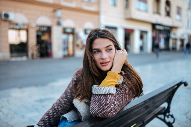 Portrait d&#39;une superbe brune assise sur le banc dans la rue.