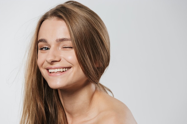 Portrait d'une superbe jeune femme blonde à moitié nue avec un clin de œil aux cheveux longs isolé sur blanc