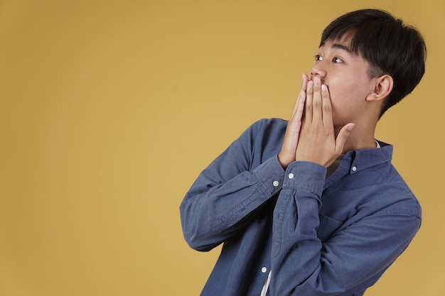 Portrait de surpris jeune homme asiatique excité habillé avec désinvolture avec les mains couvrant la bouche isolée