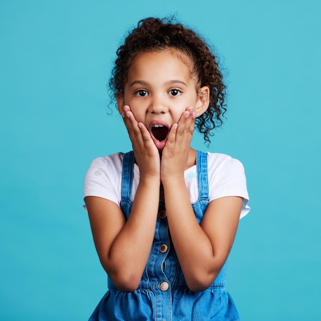 Portrait surprise et fille avec expression faciale wow et bonheur sur fond de studio bleu Visage d'enfant de sexe féminin et d'adolescent avec choc wow et halètement avec geste emoji et bonne nouvelle