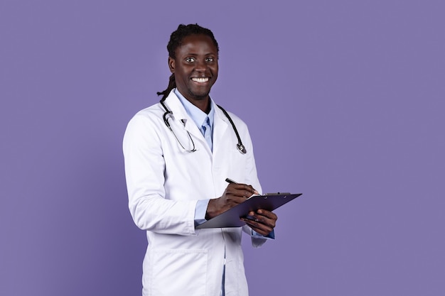 Portrait de sympathique jeune médecin afro-américain sur violet