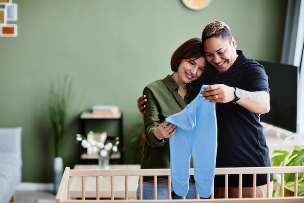 Portrait à la taille d'un couple gay heureux attendant bébé et préparant un berceau avec des vêtements de bébé à la maison sa