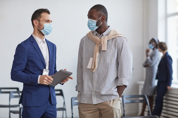 Portrait de taille de deux hommes d'affaires portant des masques et discutant pendant la pause lors d'une conférence d'affaires, espace de copie