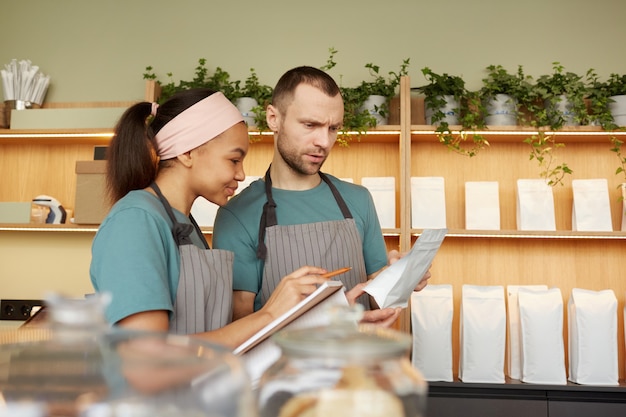 Portrait de taille de deux jeunes serveurs portant des tabliers tout en faisant l'inventaire dans un café ou un café, espace de copie