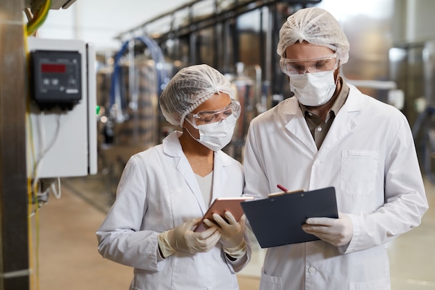 Portrait à la taille de deux travailleurs portant des masques et des blouses de laboratoire tout en discutant de la production dans une usine chimique, espace de copie