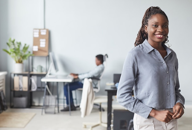 Portrait de taille d'une femme afro-américaine réussie souriant à la caméra tout en posant à l'intérieur du bureau, espace pour copie