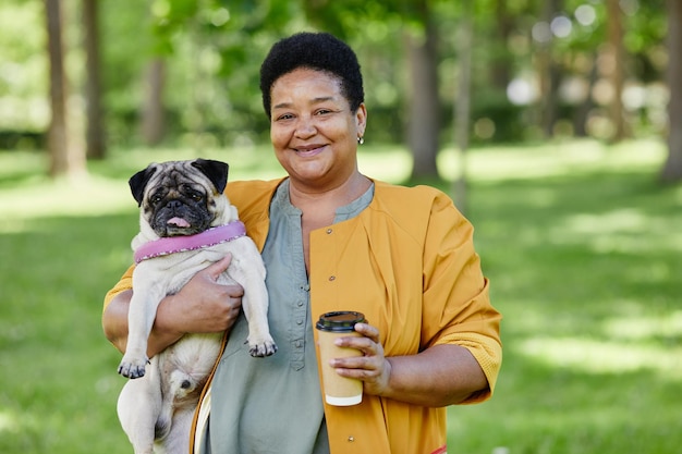 Portrait à la taille d'une femme noire mûre tenant un chien carlin mignon à l'extérieur et souriant à la caméra tout en