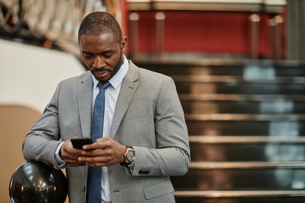 Portrait à la taille d'un homme d'affaires afro-américain à succès utilisant un smartphone dans le hall d'un hôtel luxueux, espace pour copie