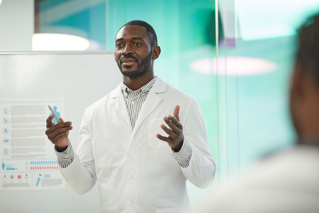 Portrait de taille d'un homme afro-américain debout près d'un tableau blanc tout en faisant une présentation lors d'un séminaire médical à l'université, espace pour copie