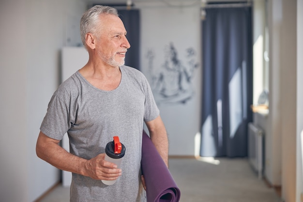 Photo portrait de taille d'un homme aux cheveux gris sportif attrayant souriant avec un tapis enroulé à l'écart