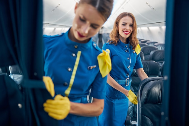 Portrait de taille d'une hôtesse de l'air amicale et heureuse, debout près des chaises confortables des passagers sur un avion commercial à grand bord