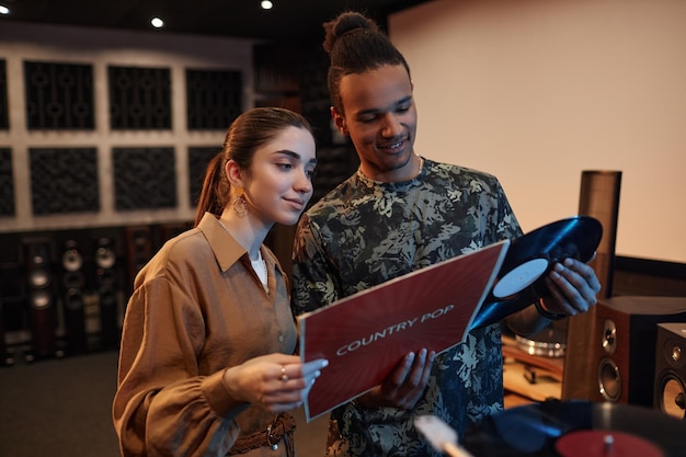 Portrait à la taille d'un jeune couple tenant des disques vnyl tout en profitant d'une soirée musicale à la maison