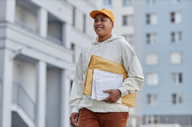 Portrait à la taille d'une jeune femme multiethnique livrant des colis en ville et souriante