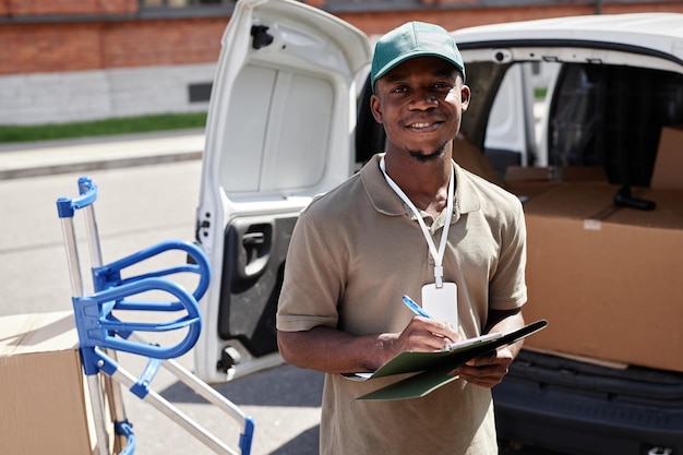 Portrait à la taille d'un jeune homme noir déchargeant une camionnette avec des colis et souriant à la caméra