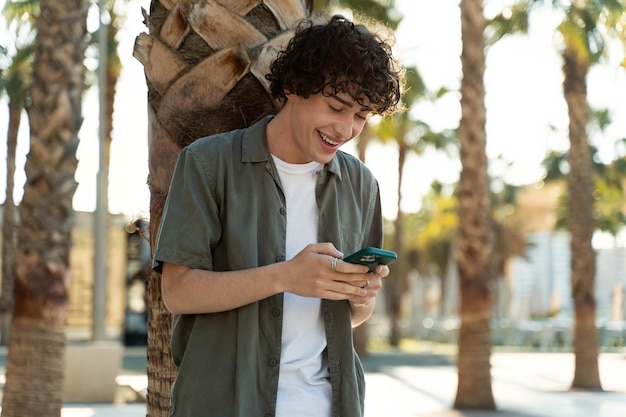 Portrait à la taille d'un jeune homme souriant aux cheveux bouclés lisant des messages sur un smartphone