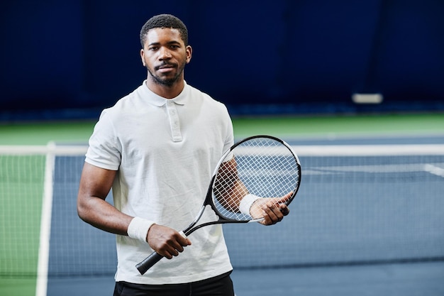 Portrait à la taille d'un joueur de tennis afro-américain regardant la caméra tout en posant en toute confiance avec