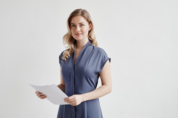 Portrait de taille minimale d'une belle femme d'affaires blonde tenant des documents et regardant la caméra ...