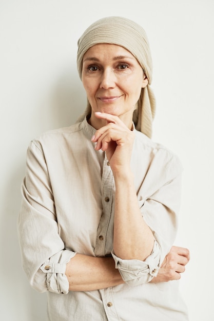 Portrait de taille minimale d'une femme mûre souriante portant un foulard et regardant la caméra en se tenant debout près d'un mur blanc