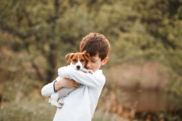 Photo portrait tendre d'un enfant garçon étreignant un chiot aimant jack russell terrier à l'extérieur