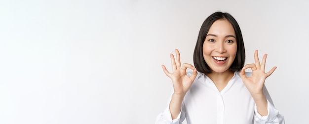 Portrait de tête en gros plan d'une fille asiatique montrant un signe correct ok et souriant satisfait recommandant d'être heureux de louer et de faire un compliment sur fond blanc