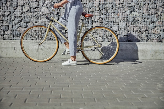 Portrait de tête recadrée d'une femme d'affaires en pantalon gris commençant à monter son vélo vintage dans la rue de la ville