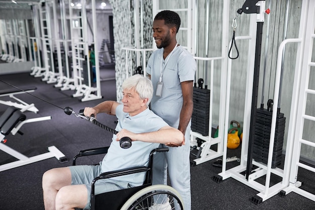 Portrait d'un thérapeute en réadaptation afro-américain aidant un homme âgé à utiliser un fauteuil roulant dans la salle de sport c