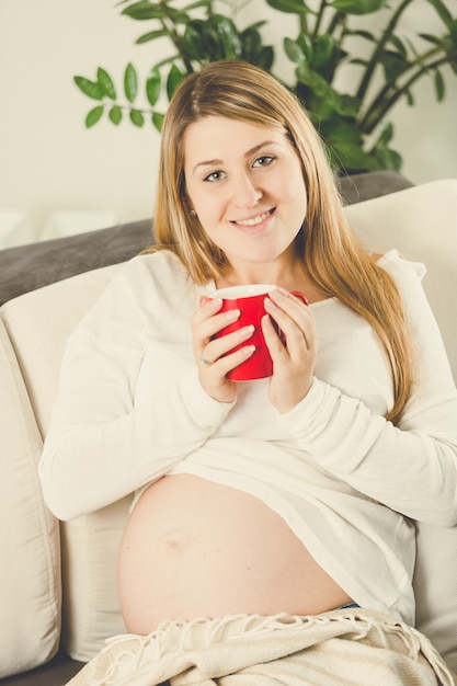 Portrait tonique d'une femme enceinte souriante heureuse assise sur un canapé avec une tasse de thé