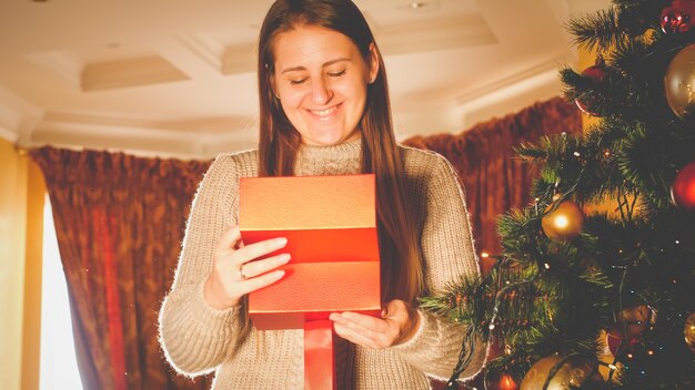 Portrait tonique d'une femme souriante heureuse regardant à l'intérieur de la boîte-cadeau de Noël