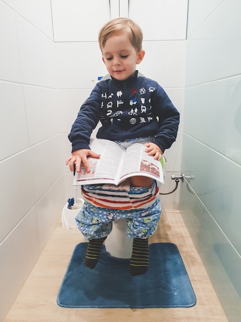 Portrait Tonique D'un Petit Garçon Intelligent Se Tenant Sur Les Toilettes Et Lisant Des Magizines