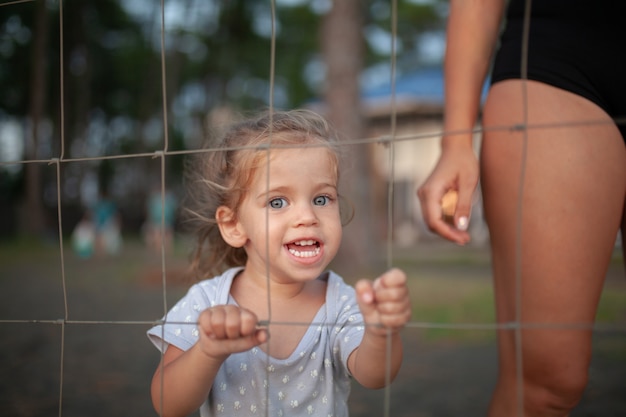 Portrait tonique de la petite fille triste regarde à travers une clôture métallique