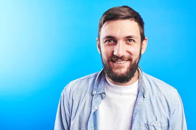 Portrait de toothy souriant et riant joyeusement beau caucasien brutal barbu habillé en décontracté isolé sur fond bleu