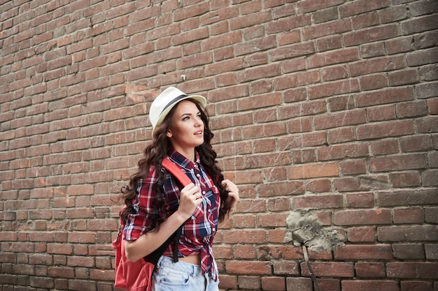 Portrait d'une touriste de fille dans un chapeau sur un fond de bâtiment de brique rouge
