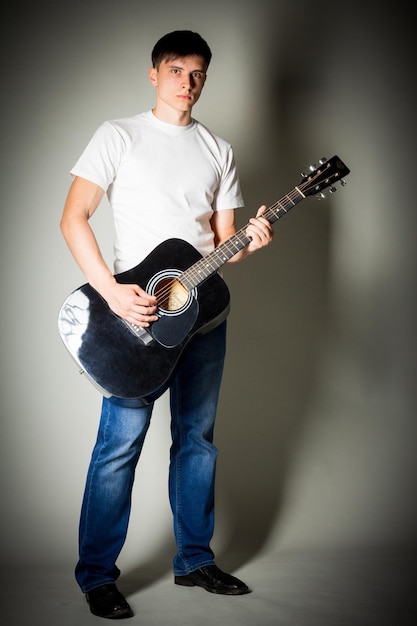 Portrait de toute la longueur d'un beau jeune homme debout avec une guitare dans la chambre