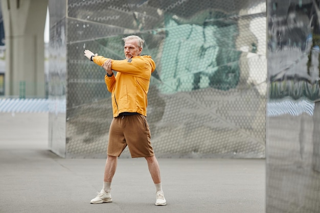 Portrait de toute la longueur d'un bel homme mûr faisant des exercices d'étirement à l'extérieur dans la ville urbaine