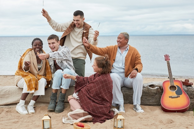 Portrait de toute la longueur d'un groupe de jeunes branchés profitant d'une fête sur la plage en automne et tenant s...