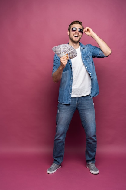 Portrait De Toute La Longueur D'un Homme Joyeux En Chemise De Jeans Tenant Un Tas De Billets D'argent En Se Tenant Debout Et En Célébrant Isolé Sur Fond Rose