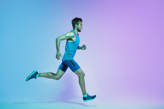 Portrait de toute la longueur d'un jeune caucasien actif en cours d'exécution, homme de jogging sur fond de néon