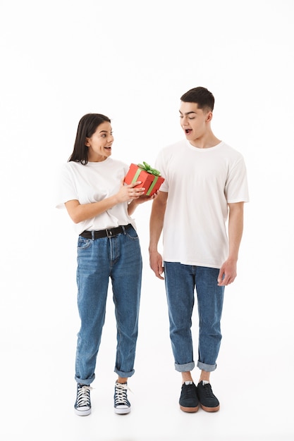 Portrait de toute la longueur d'un jeune couple séduisant debout isolé sur un mur blanc, donnant une boîte présente