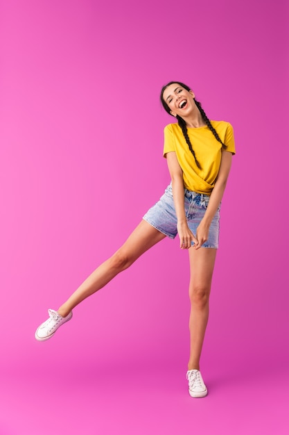 Portrait de toute la longueur d'une jeune femme joyeuse portant un short en jean s'amusant et dansant isolé sur un mur rose