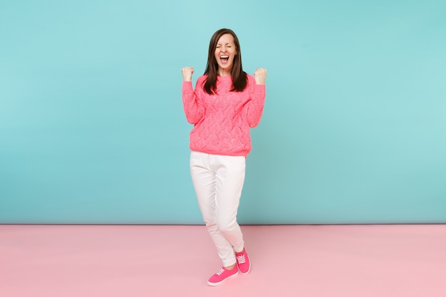 Portrait de toute la longueur d'une jeune femme souriante en pull rose tricoté, pantalon blanc posant